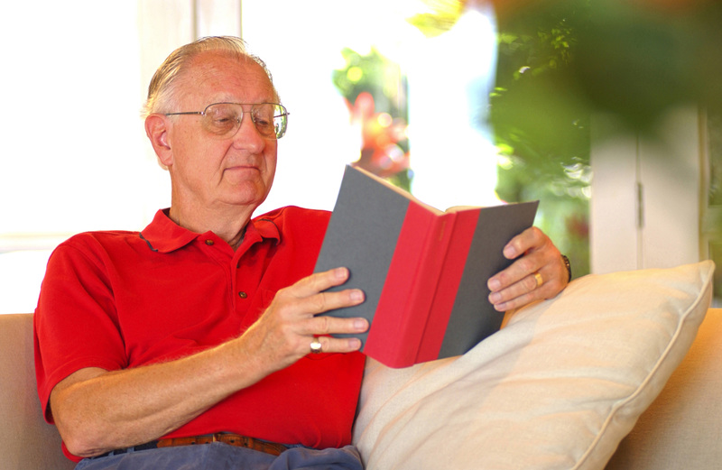عکس، یک مرد بالغ قفقازی که روی مبل نشسته و مشغول خواندن کتاب رنگی است