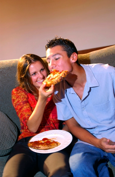 عکس، زوج نوجوان نشسته روی مبل در حال خوردن پیتزا، رنگی