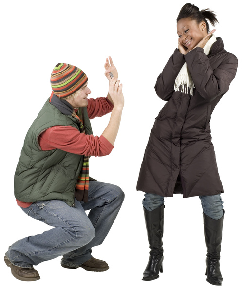 مرد جوانی که لباس زمستانی پوشیده و با تلفن همراه از زن جوان عکس می گیرد