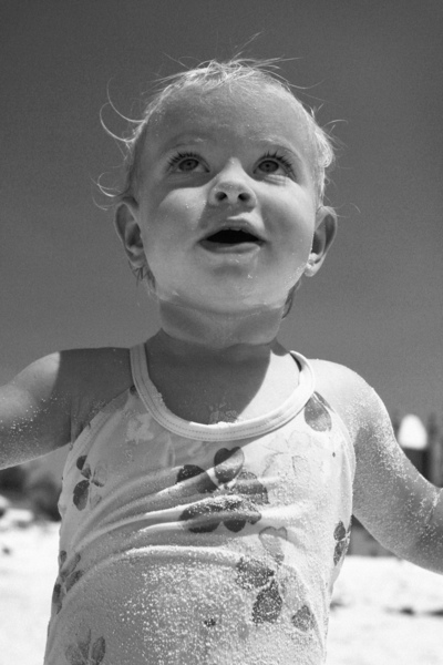 عکس سیاه و سفید یک نوزاد دختر قفقازی با لباس شنا در حالی که در ساحل بازی می کند